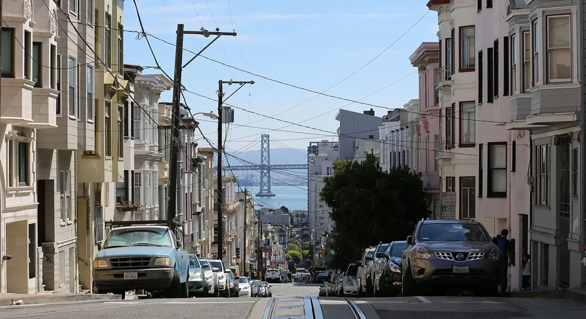 Row of San Francisco Victorian homes on a hill with the Bay Bridge behind them